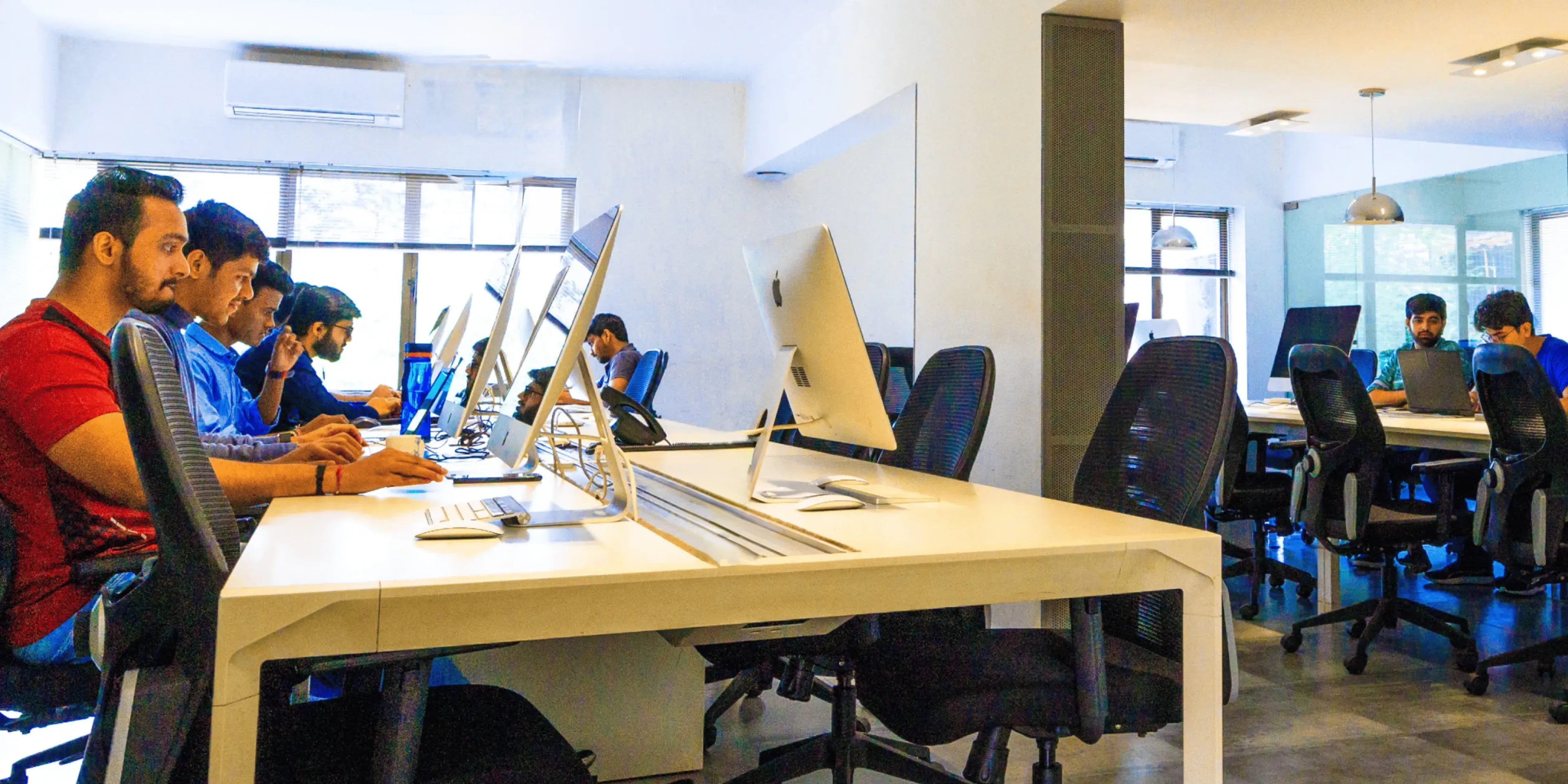 A group of professionals working at a modern office in Mumbai, India, using Apple desktop computers. The workspace has large windows and a vibrant atmosphere, showcasing innovation and productivity.